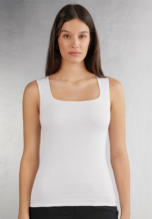 Witte mouwloze top met een vierkante halslijn, strakke pasvorm, gladde textuur en minimale details, gecombineerd met donkere broek.