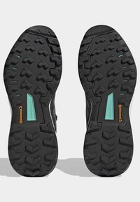 Suole di scarpe da trail nere con un disegno del battistrada robusto, dotate di una piastra protettiva verde e marchio Continental per una migliore trazione.