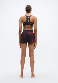 Brassière de sport noire et rouge et short assorti avec un motif texturé. La brassière comporte un logo dans le dos ; le short a une ceinture confortable.
