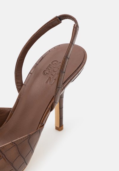 Rjava, usnjena slingback višina s potiskom krokodila in ozkim trakom ter tankim, svetlim lesenim stiletto peto. Teksturirana podloga s logotipom.