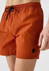 Pantaloni da nuoto arancioni realizzati in tessuto leggero, con motivo a griglia, vita elastica con cordoncino nero e accenti del logo nero.