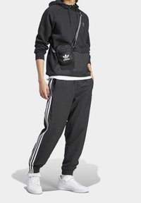 Svart hoodie med justerbar huva, tillsammans med svarta träningsbyxor med vita sidostripes. Vita sneakers avslutar looken.