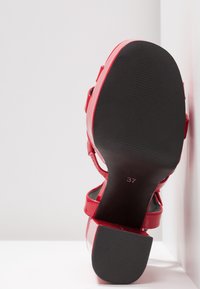 Sandale à talons hauts en cuir verni rouge, avec un orteil ouvert, une sangle ajustable et une semelle texturée noire ; taille marquée comme 37.
