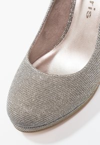 Escarpin en métal argenté avec texture striée, bout rond et doublure intérieure douce. Présente un subtil éclat et des finitions lisses autour de l'ouverture.