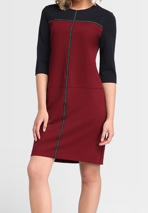 Robe avec un corps bordeaux et des manches noires, fermée par un zip à l'avant, accentuée par une couture décorative le long du zipper.