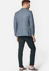 Marynarka w kratę w odcieniach niebieskiego i szarego o dopasowanym kroju, zestawiona z ciemnozielonymi chinosami i szarymi sneakersami, widok z tyłu.