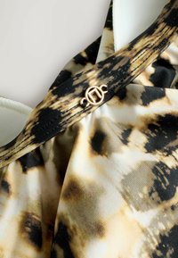 Zwart en beige gestoffeerd textiel met een zachte textuur. Bevat een decoratieve gouden hardware-detail op de band.