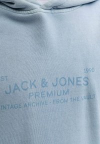 Svetlomodrá mikina Jack & Jones Premium s jemným potlačeným textom "Vintage Archive - From The Vault 1990" na prednej strane látky.