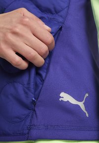 Violet spalvų sportinė liemenė su pagalvėlėmis, turinti sidabrinį logotipą, užtrauktuką ir mažą mėlyną mygtuko detalę šone.