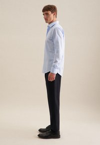 Camicia button-up azzurra con colletto classico, maniche lunghe e polsini, abbinata a pantaloni scuri e scarpe nere.