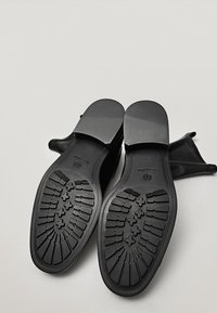 Chaussures noires avec semelles en caoutchouc texturé, avec un dessus lisse et un design à bout rond. La semelle a un grip à motif pour une traction accrue.