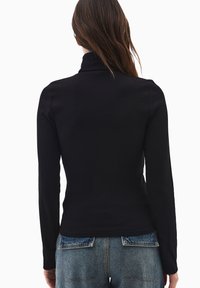 Czarny sweter z długim rękawem i golfem, o prążkowanej fakturze, dopasowany krój i delikatnie zaokrąglony dół, zestawiony z jasnoniebieskimi spodniami o wysokim stanie.