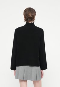 Suéter de punto negro con cuello alto y mangas largas, combinado con una falda plisada gris. La textura parece suave y lisa.