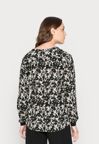Blusa preta com padrão floral branco, mangas compridas, decote redondo e detalhe franzido nos ombros e punhos. Textura de tecido macio.