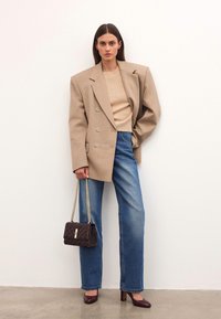 Blazer beige doppiopetto, maglione beige a costine, jeans blu a vita alta, borsa trapuntata marrone, tacchi bordeaux. Texture lisce e design strutturato.