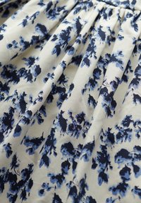 Hvidt stof med blåt og marineblåt blomsterprint, der viser bløde folder og tekstur.