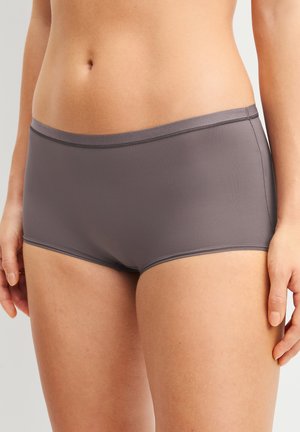 Frau trägt graue nahtlose Hipster-Unterwäsche, zeigt Taille, Hüften und obere Oberschenkel vor einfarbigem Hintergrund.