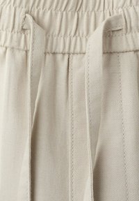 Pantaloni in tessuto di cotone beige con vita elastica e cordoncino piatto davanti, che mostra la trama testurizzata e dettagli di cucitura.