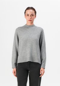 Grauer Strickpullover mit hohem Kragen, gerippten Bündchen und Saum, mit einer lockeren Passform und weichem Material, kombiniert mit schwarzen Jeans.
