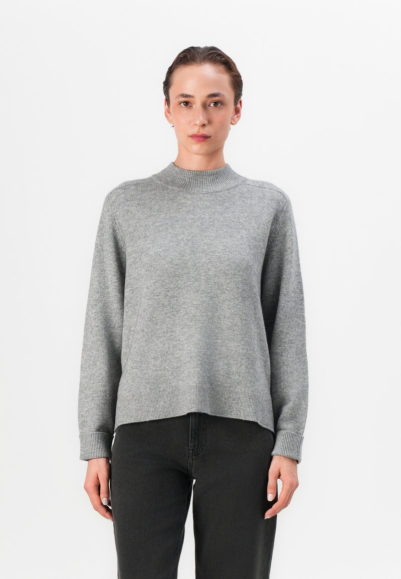 Grauer Strickpullover mit hohem Kragen, gerippten Bündchen und Saum, mit einer lockeren Passform und weichem Material, kombiniert mit schwarzen Jeans.