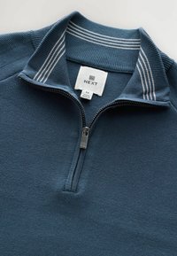 Pulover pentru bărbați, de culoare albastră închis, cu fermoar pe un sfert. Material texturat, guler cu benzile ondulate albe. Eticheta prinsă indică marca și mărimea.
