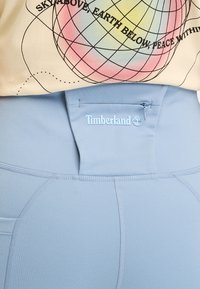 Ljusblåa träningsbyxor med hög midja och Timberland-logotyp, slät textur och platta sömmar för komfort.