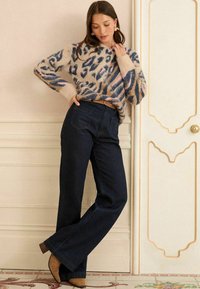 Bežs dzīvnieku raksta džemperis ar garām piedurknēm, apvienots ar augsto jostasvietu zilo džinsu un brūniem papēžu zābakiem. Vienkārša jostas akcenta detaļa.