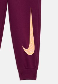 Bordo trenirke s rebrastim manžetama, s narančastim Nike logotipom s valovitim uzorkom na lijevoj strani. Mekana tekstura.