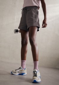 Pantalones cortos de algodón grises con cintura ajustable, calcetines deportivos rosas y zapatillas beige-azul. Longitud corta y diseño casual con detalle de logo.
