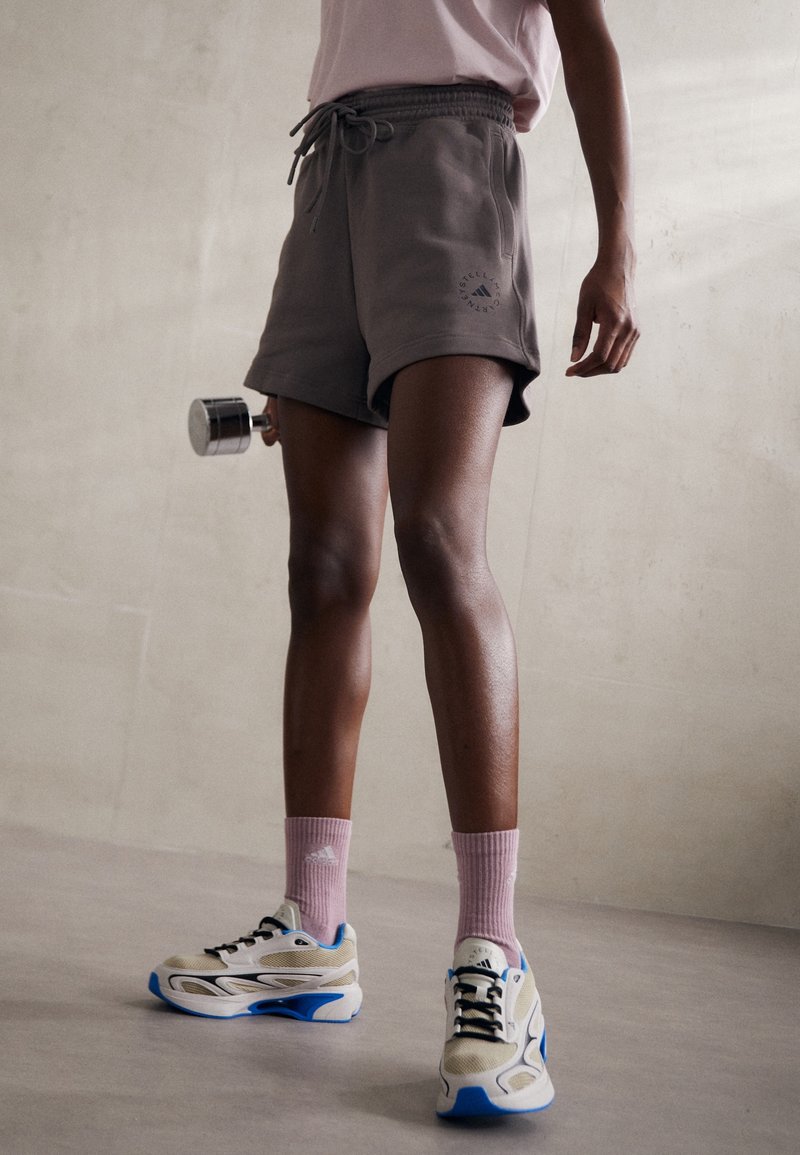 Pantalones cortos de algodón grises con cintura ajustable, calcetines deportivos rosas y zapatillas beige-azul. Longitud corta y diseño casual con detalle de logo.
