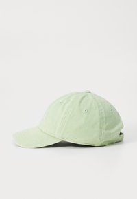 Svetlo zelena bombažna baseball kapa z ukrivljenim ščitnikom in nastavljivim trakom, prikazana od strani na belem ozadju.