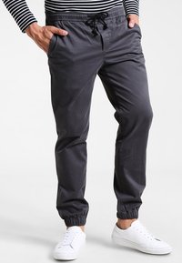 Pantalon de jogging gris charbon en matière douce, doté d'une ceinture élastique avec cordon de serrage, de poches latérales et de poignets élastiques.
