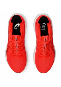 Baskets de sport rouges avec une tige en maille texturée, logo noir et semelle blanche. Elles présentent des lacets plats et une languette rembourrée.