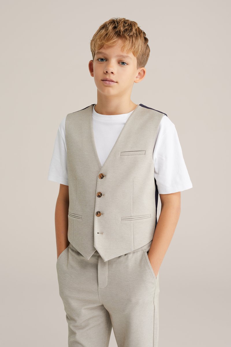 Grau strukturierte Weste mit drei Holzknöpfen und Taschenakzenten, getragen über einem weißen T-Shirt, kombiniert mit passenden grauen Hosen.