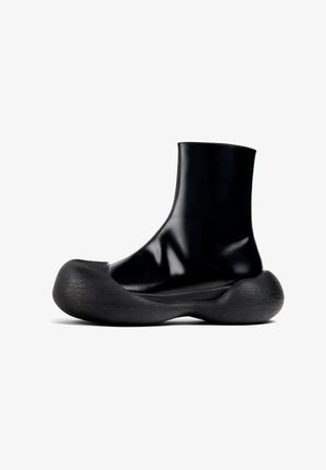 Bottes noires à la cheville en matériau brillant, avec une semelle arrondie en caoutchouc texturé et un design lisse et haut.