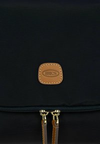 Borsa in tessuto nero con superficie testurizzata, dotata di una patch con logo in pelle marrone e cerniere color oro. Due tirazip in pelle.