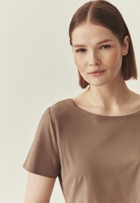 Haut marron à manches courtes avec un col rond, confectionné dans un tissu lisse et léger. Présente une coupe décontractée et un design minimaliste.