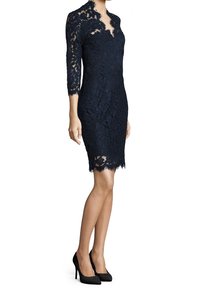 Robe en dentelle bleu marine jusqu'aux genoux avec des manches trois-quarts et des bords festonnés, portée avec des chaussures à talons hauts noires.