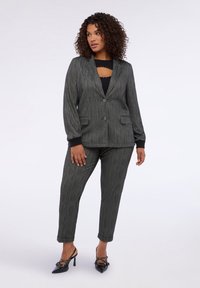 Šedý pruhovaný oblek s upraveným sakem a úzkými kalhotami, které mají dvě přední kapsy a černé lemování. Pár černých lodiček s ozdobami.