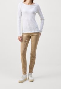 Haut blanc à manches longues avec un col dégagé, associé à un pantalon beige ajusté et des baskets blanches avec une semelle texturée.