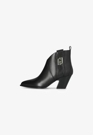 Stivaletto in pelle nera con punta appuntita, tacco medio e logo in metallo decorativo sul lato. Texture liscia e design elegante.