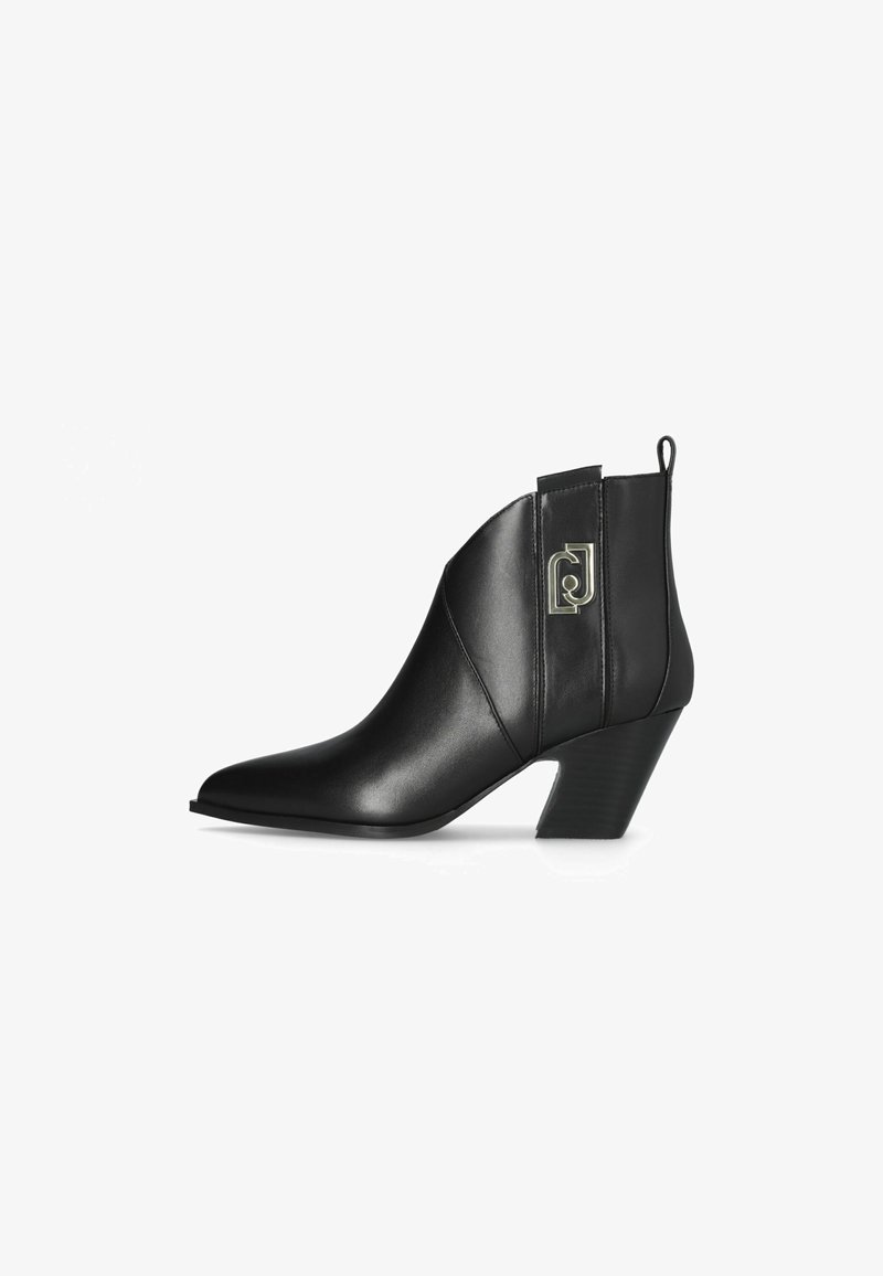 Stivaletto in pelle nera con punta appuntita, tacco medio e logo in metallo decorativo sul lato. Texture liscia e design elegante.