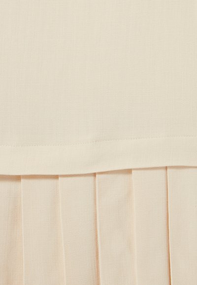 Tela plisada de un beige claro con una superficie texturada, que presenta una sección superior suave y pliegues verticales distintivos que aportan una estructura general.