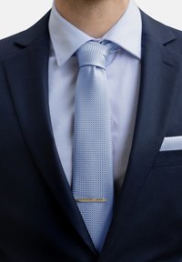 Giacca di abito blu navy con una camicia formale azzurro chiaro e una cravatta azzurro chiaro a fantasia, con un fermacravatta d'argento, ordinatamente sistemato al colletto.