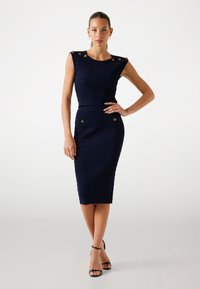 Robe midi côtelée marine avec boutons d'épaule, design ajusté et poches avant. Texture lisse avec une silhouette structurée.