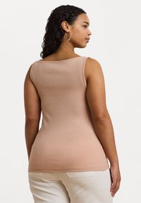 Ljusrosa ribbad linne med rundad halsringning, figursydd passform och en slät textur, matchad med ljusbeiga byxor.