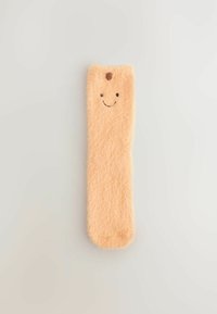 Weiche pfirsichfarbene flauschige Socke mit einem kleinen braunen Fleck und einem einfachen, lächelnden Gesicht, das nahe der oberen Kante auf einem schlichten Hintergrund gestickt ist.