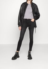 Chaqueta bomber de cuero sintético negra con puños acanalados, camiseta gris claro, vaqueros skinny de tiro alto negros y botas de tobillo negras.