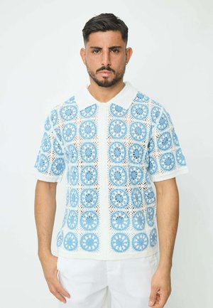 Polo en crochet blanc et bleu clair, affichant des motifs circulaires et des manches courtes, avec un col blanc contrastant et une fermeture à boutons.