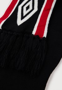 Crni šal s bijelim i crvenim dijamantnim uzorcima, naglašen bijelim i crvenim prugama, s dugim crnim resicama na jednom kraju.